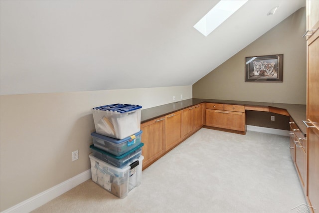 office area featuring lofted ceiling with skylight, light carpet, and built in desk