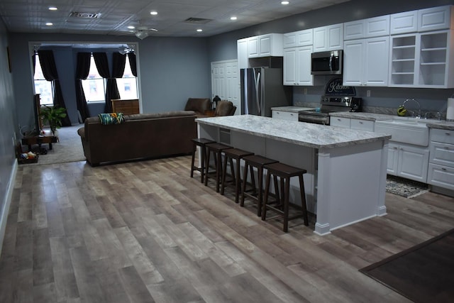 kitchen with a center island, light stone countertops, a kitchen breakfast bar, stainless steel appliances, and white cabinets