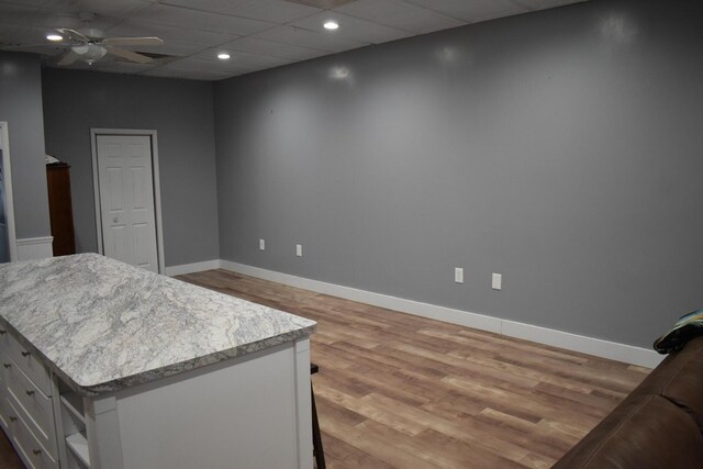 interior space with ceiling fan, a center island, white cabinetry, hardwood / wood-style flooring, and a paneled ceiling