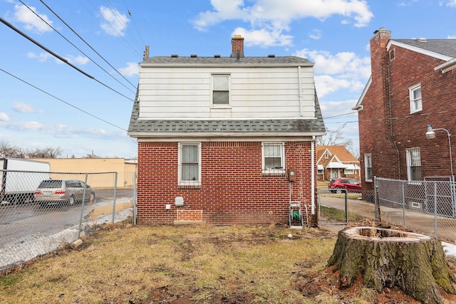 rear view of property featuring a yard, brick siding, fence, and roof with shingles