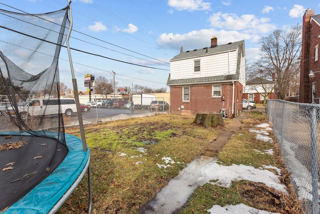 exterior space with a chimney, a trampoline, fence, and brick siding