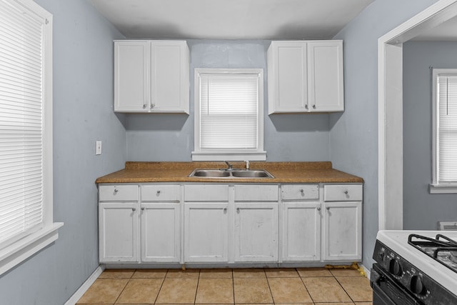 kitchen with light tile patterned floors, white cabinets, a sink, and range with gas cooktop