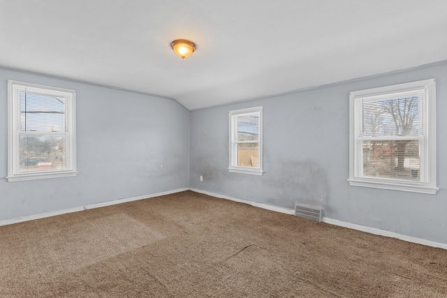 carpeted spare room with visible vents, vaulted ceiling, and a wealth of natural light