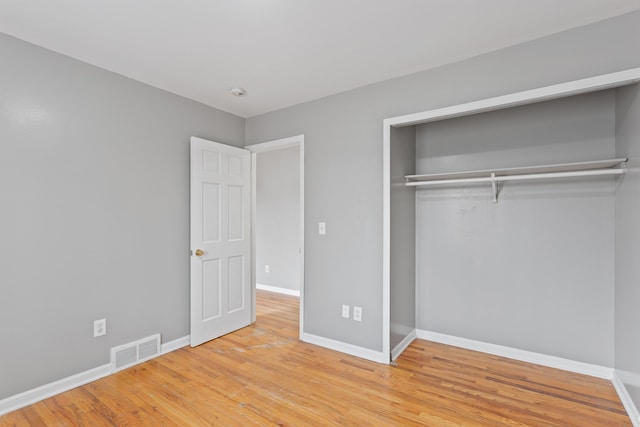 unfurnished bedroom featuring wood finished floors, visible vents, a closet, and baseboards