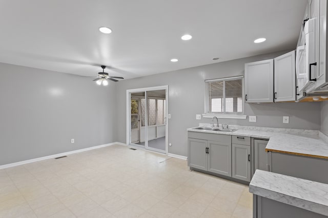 kitchen with baseboards, light countertops, recessed lighting, gray cabinets, and a sink