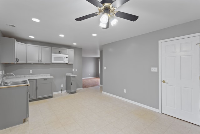 kitchen with white microwave, baseboards, recessed lighting, gray cabinetry, and a sink