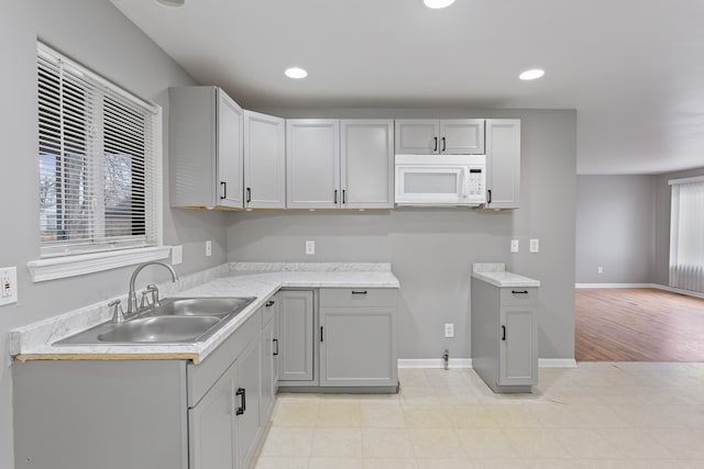 kitchen featuring gray cabinets, a sink, recessed lighting, baseboards, and white microwave