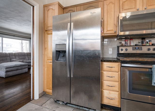 kitchen featuring appliances with stainless steel finishes, dark stone countertops, backsplash, light tile patterned floors, and light brown cabinets