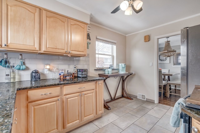 kitchen with ornamental molding, dark stone countertops, light brown cabinetry, and backsplash