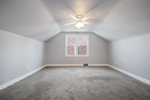 additional living space with ceiling fan, lofted ceiling, carpet flooring, and a textured ceiling