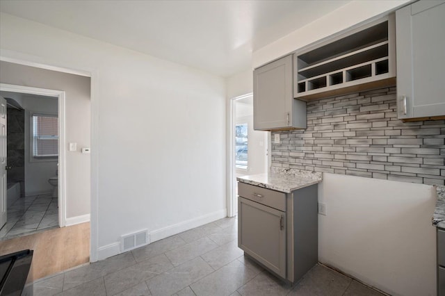 kitchen featuring light stone counters, gray cabinets, tasteful backsplash, and light tile patterned floors