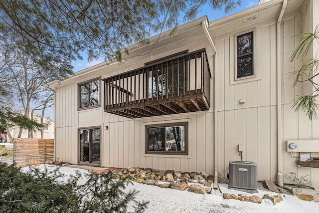 snow covered back of property with central AC unit and a balcony