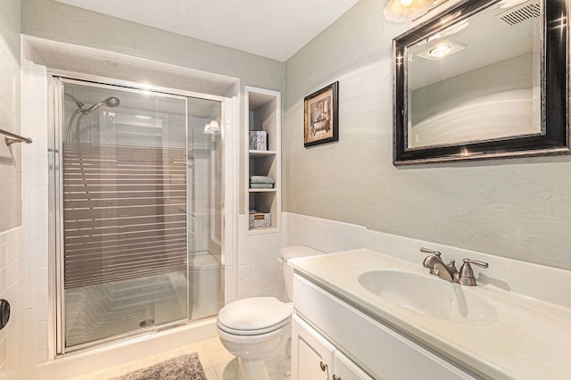 bathroom featuring tile patterned flooring, vanity, tile walls, toilet, and walk in shower