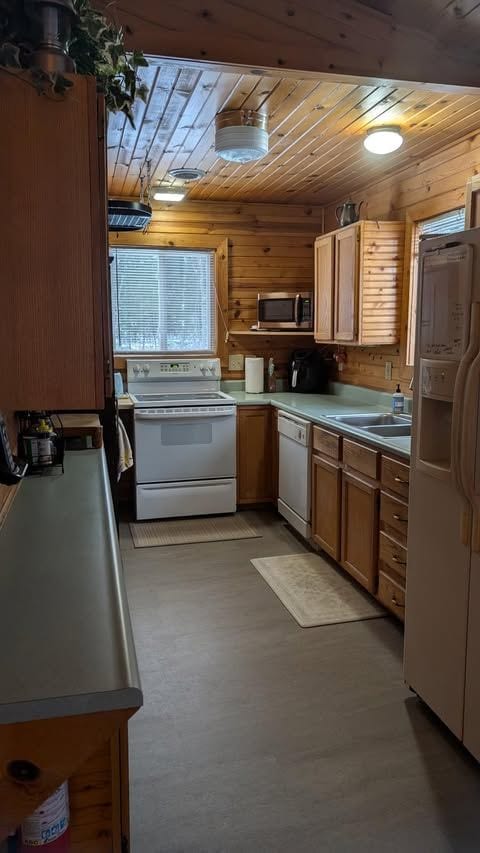 kitchen with wood walls, wooden ceiling, white appliances, and sink