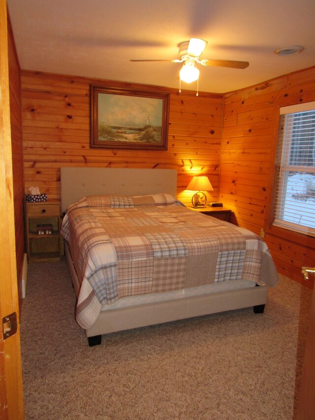 carpeted bedroom with ceiling fan and wood walls