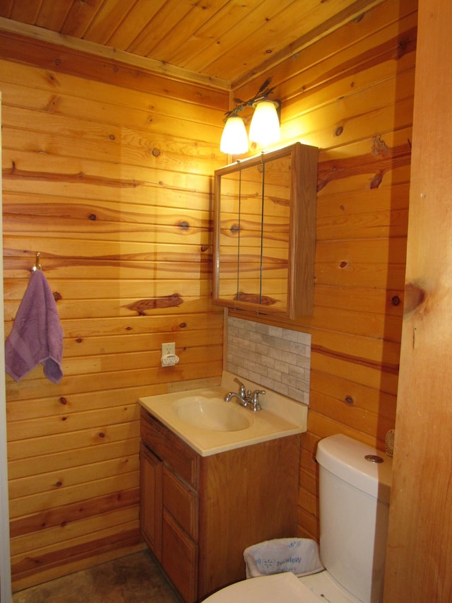 bathroom with vanity, toilet, wooden walls, and wooden ceiling