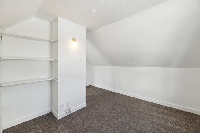 additional living space with vaulted ceiling, a textured ceiling, and dark carpet