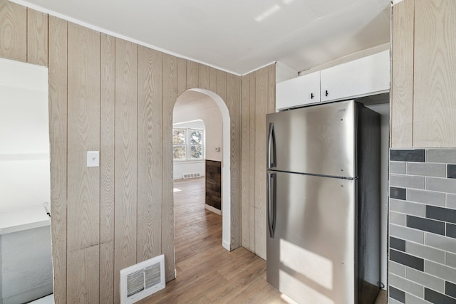 kitchen with white cabinetry, stainless steel fridge, light hardwood / wood-style flooring, and wood walls