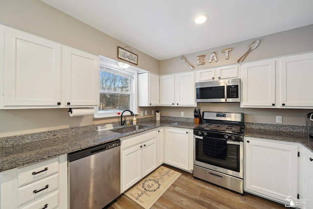 kitchen with white cabinetry, stainless steel appliances, dark stone counters, light hardwood / wood-style floors, and sink