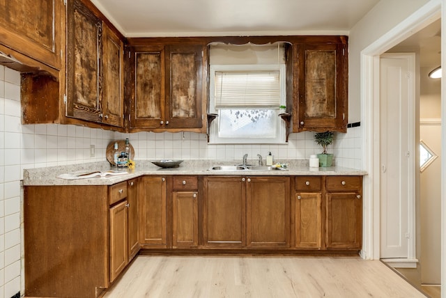 kitchen featuring sink, light wood-type flooring, light stone countertops, and decorative backsplash