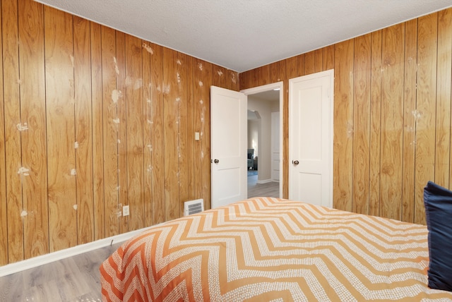 bedroom featuring a textured ceiling, wood-type flooring, and wooden walls