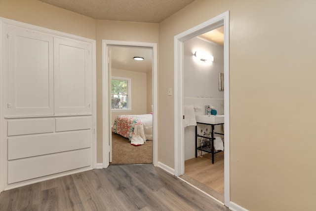 corridor featuring sink, light wood-type flooring, and a textured ceiling