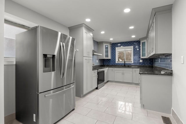 kitchen featuring appliances with stainless steel finishes, decorative backsplash, gray cabinetry, sink, and dark stone counters