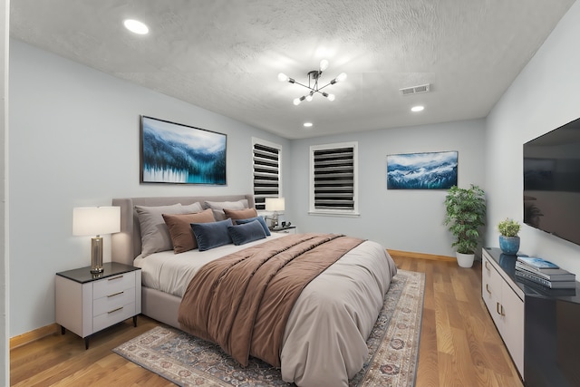 bedroom with light wood-type flooring, a textured ceiling, and a notable chandelier