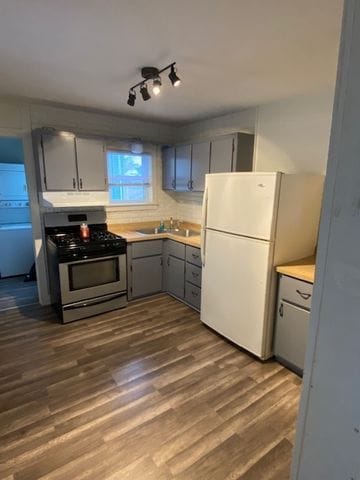 kitchen with gas stove, dark wood-type flooring, white refrigerator, sink, and gray cabinets