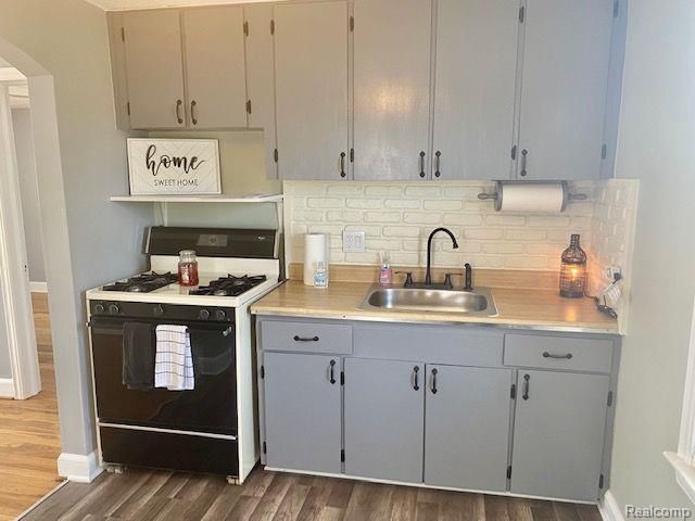 kitchen featuring range with gas stovetop, sink, dark wood-type flooring, backsplash, and gray cabinets