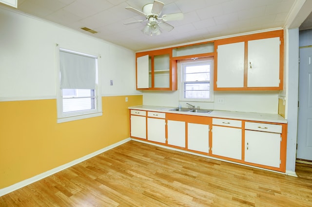 kitchen with white cabinetry, sink, light hardwood / wood-style flooring, ornamental molding, and ceiling fan