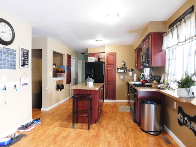 kitchen featuring a center island, range with gas stovetop, black fridge, light wood-type flooring, and a breakfast bar area