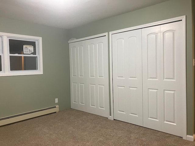 unfurnished bedroom featuring a baseboard radiator, light colored carpet, and two closets