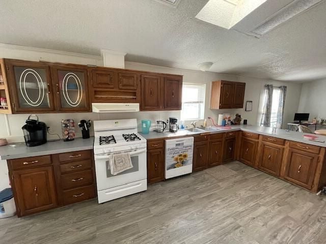 kitchen featuring dishwashing machine, a textured ceiling, white range with gas cooktop, a skylight, and light hardwood / wood-style floors