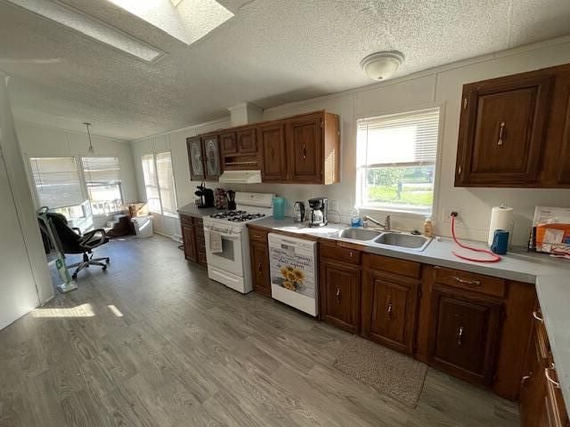 kitchen with pendant lighting, sink, light wood-type flooring, white appliances, and vaulted ceiling with skylight