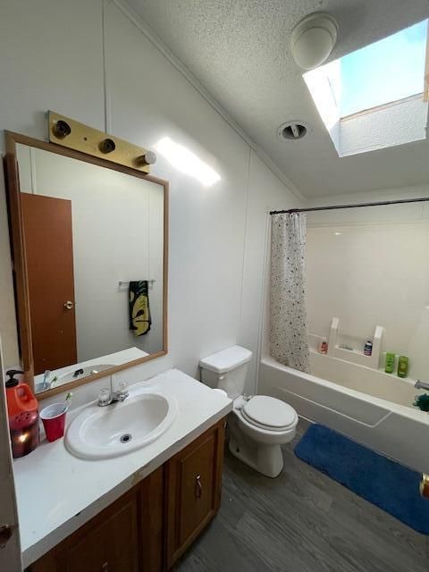 full bathroom featuring wood-type flooring, toilet, a textured ceiling, vanity, and shower / bathtub combination with curtain