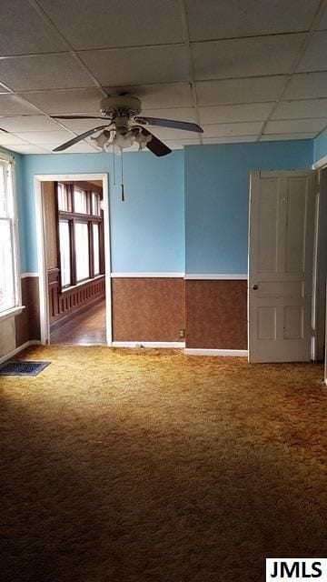 carpeted empty room featuring ceiling fan and a paneled ceiling