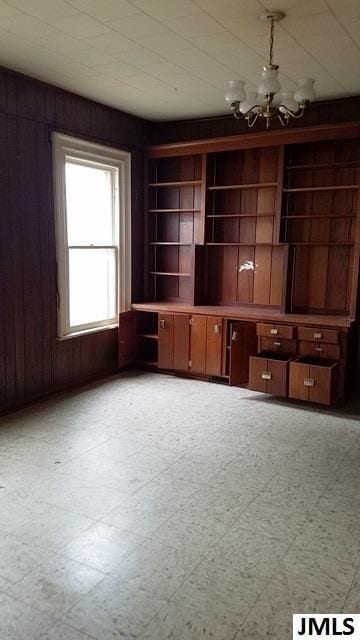 unfurnished office featuring built in shelves, wood walls, and an inviting chandelier