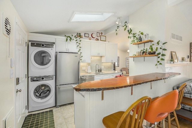 interior space featuring sink, stacked washer and dryer, a breakfast bar area, stainless steel appliances, and white cabinets