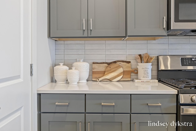 details with tasteful backsplash, appliances with stainless steel finishes, light countertops, and gray cabinetry