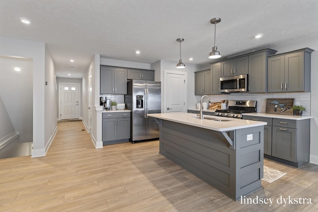 kitchen featuring light wood-style flooring, a sink, gray cabinetry, light countertops, and stainless steel appliances