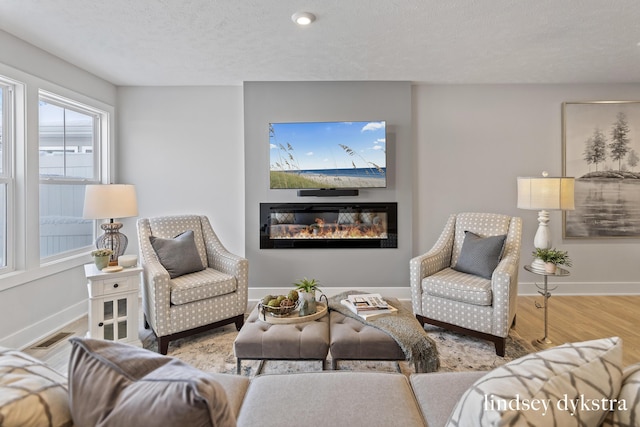 living area with visible vents, baseboards, wood finished floors, a glass covered fireplace, and a textured ceiling