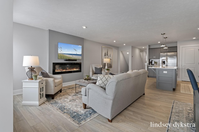 living room featuring baseboards, light wood-style floors, a glass covered fireplace, and a textured ceiling