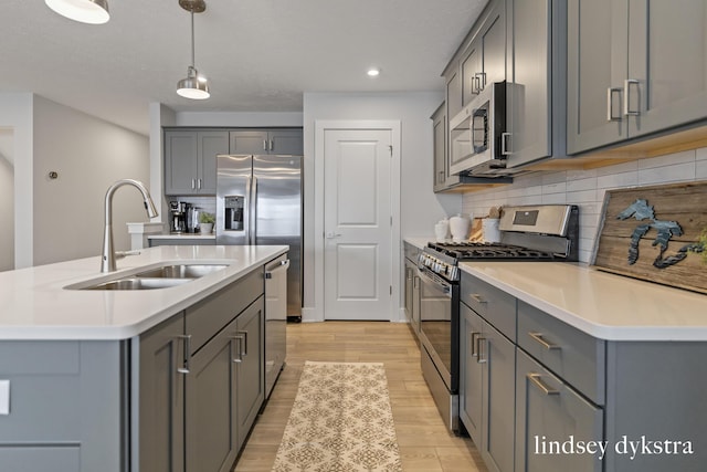 kitchen featuring light wood-style flooring, gray cabinets, a sink, stainless steel appliances, and backsplash