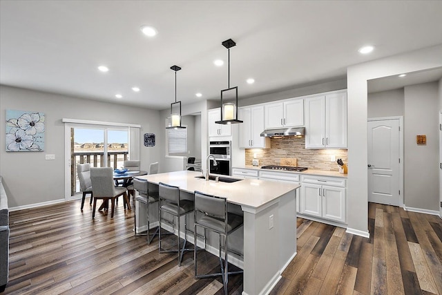 kitchen featuring decorative light fixtures, tasteful backsplash, white cabinetry, a kitchen island with sink, and stainless steel appliances