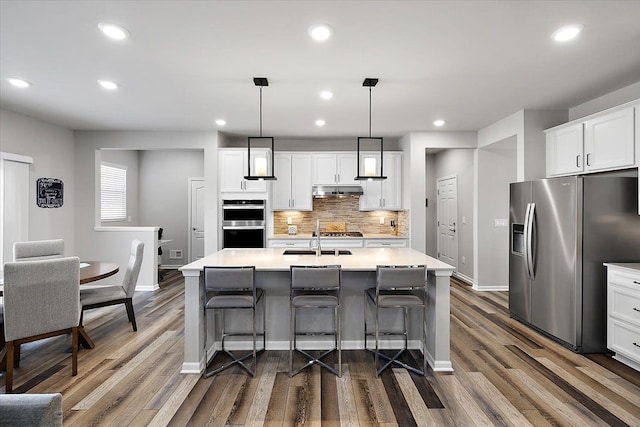 kitchen featuring white cabinetry, hanging light fixtures, a center island with sink, and appliances with stainless steel finishes