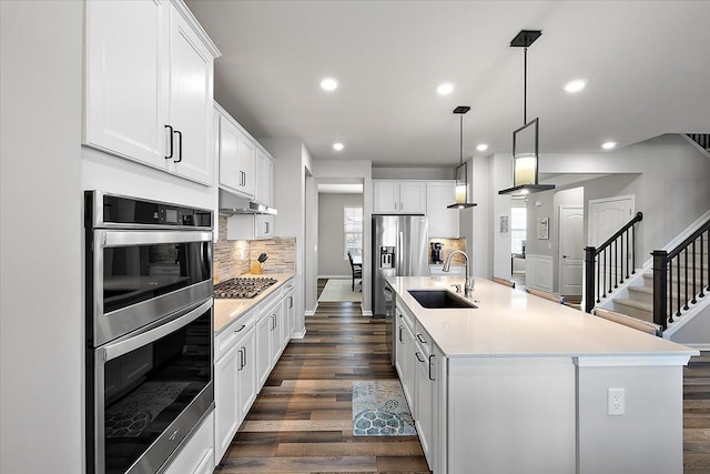 kitchen with appliances with stainless steel finishes, pendant lighting, an island with sink, sink, and white cabinets