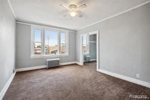 empty room featuring ceiling fan, radiator heating unit, crown molding, and dark carpet