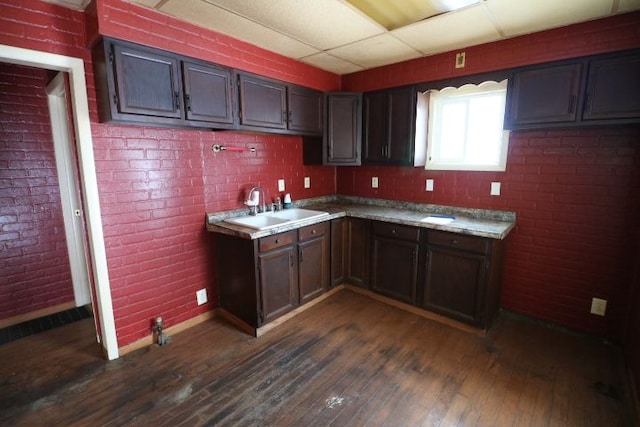 kitchen featuring brick wall, sink, a paneled ceiling, and dark wood-type flooring