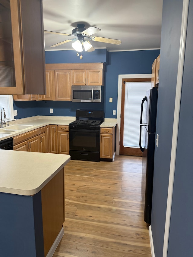 kitchen featuring light countertops, light wood-style floors, a ceiling fan, a sink, and black appliances